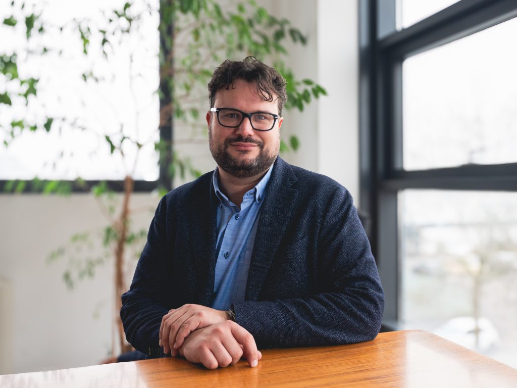 Isinet Consulting Professionista seduto in un ufficio moderno, con piante verdi sullo sfondo, esprimendo un'immagine di competenza e serietà.