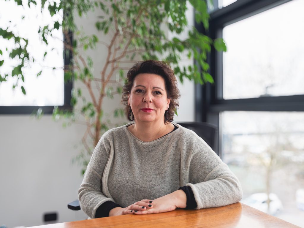 Isinet Consulting Una donna professionale seduta a un tavolo in un ambiente luminoso, circondata da piante verdi.