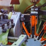 Isinet Consulting Dettaglio ravvicinato di un macchinario industriale con componenti meccaniche arancioni e metalliche, ideale per Bando Metalmeccanica 2026 Veneto.