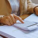 Isinet Consulting Una persona utilizza una calcolatrice mentre lavora su un computer portatile e documenti aziendali.