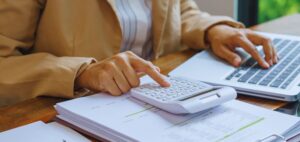 Isinet Consulting Una persona utilizza una calcolatrice mentre lavora su un computer portatile e documenti aziendali.