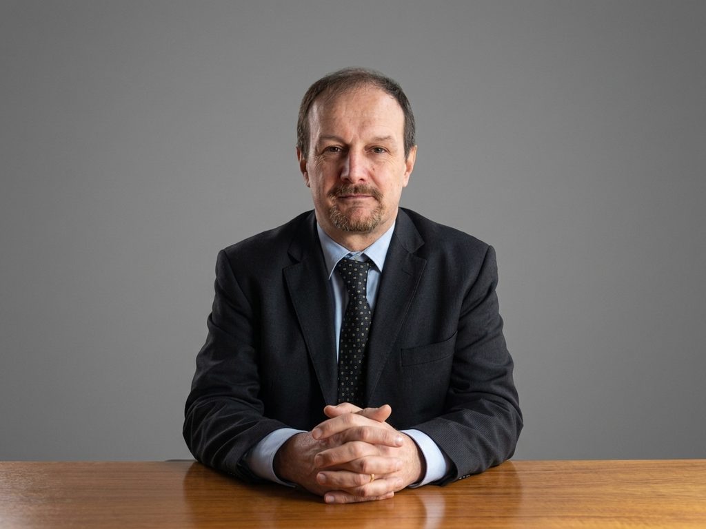 Isinet Consulting Un professionista maturo in giacca e cravatta siede a un tavolo in legno, rappresentando l'Ufficio Studi in un contesto aziendale formale.