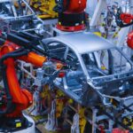 Isinet Consulting Bracci robotici industriali rossi lavorano sulla scocca di un'auto in una fabbrica moderna, tema centrale per Accordi per l’innovazione automotive 2026.