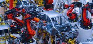 Isinet Consulting Bracci robotici industriali rossi lavorano sulla scocca di un'auto in una fabbrica moderna, tema centrale per Accordi per l’innovazione automotive 2026.