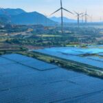 Isinet Consulting Un vasto parco solare con numerosi pannelli fotovoltaici e turbine eoliche in un paesaggio collinare, ideale per SIMEST energivore 2026 e Misura Energia.
